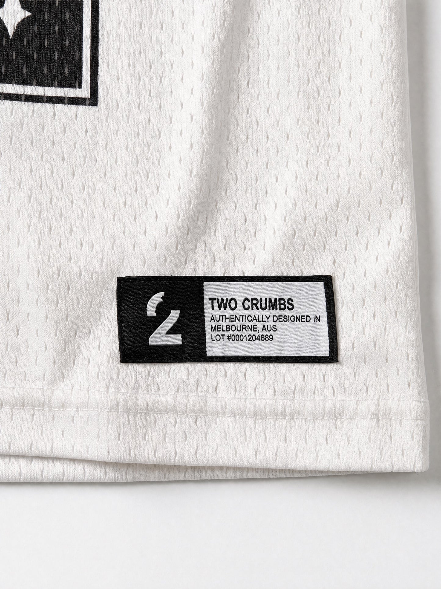 Two Crumbs mesh jersey tee in white — hem tag detail, woven label with brand and lot number