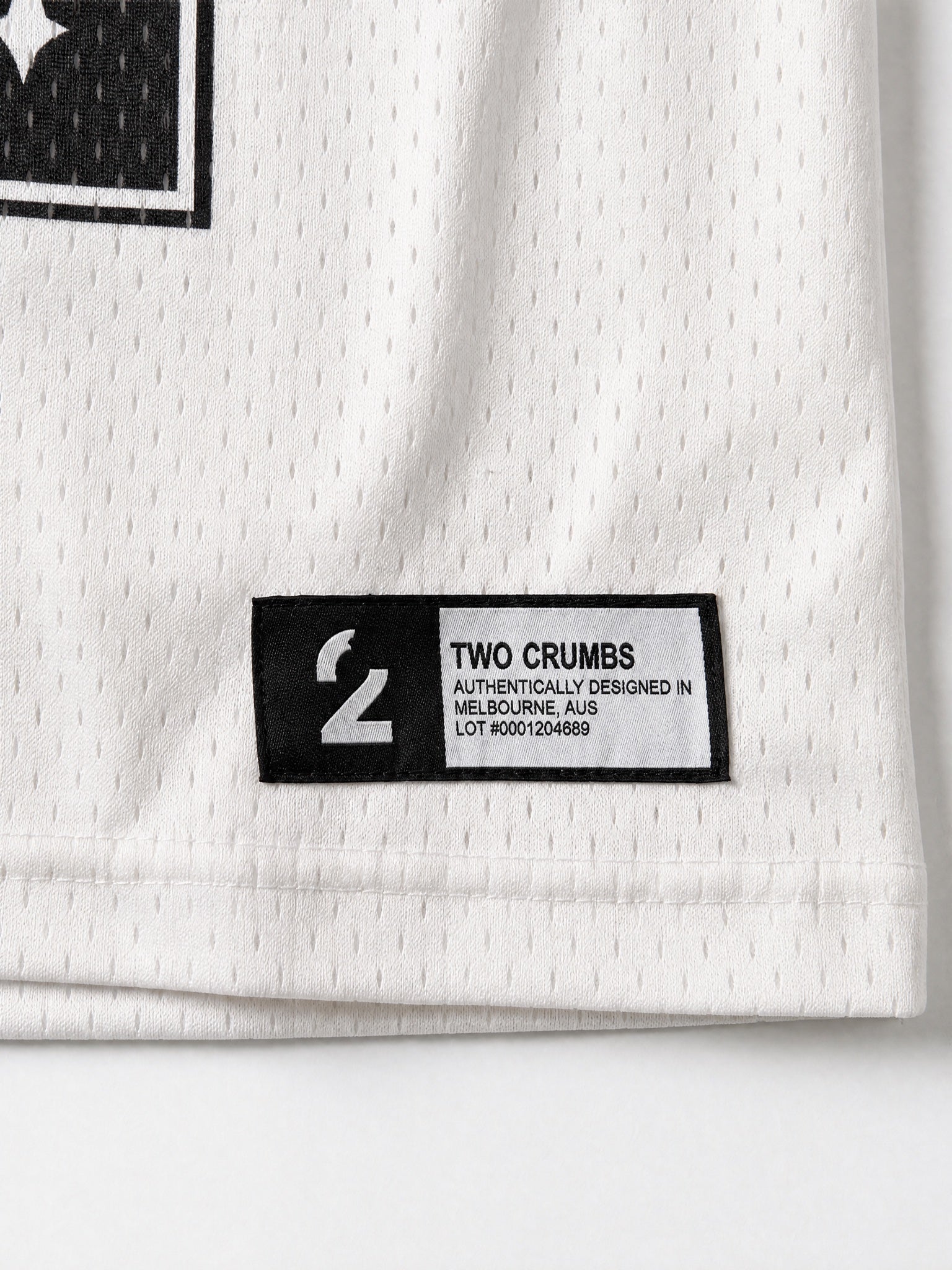 Two Crumbs mesh jersey tee in white — hem tag detail, woven label with brand and lot number